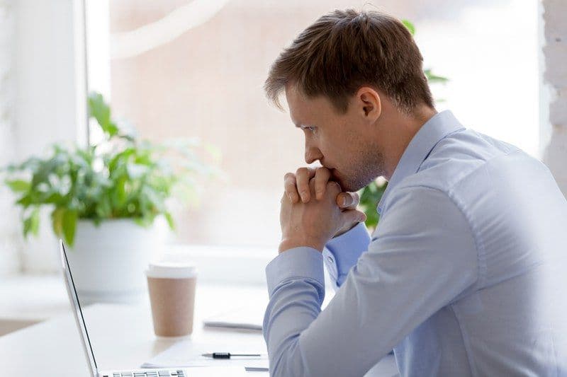 A man is sitting at a table with his hands on his chin.